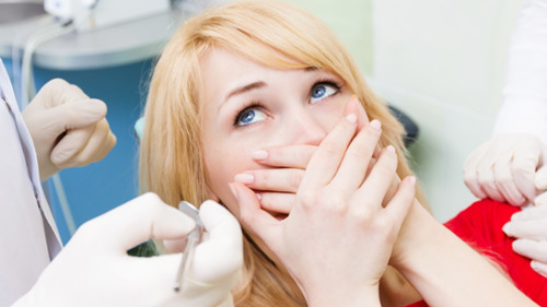 Anxious woman covering her mouth in a dental chair as dentist approaches with instruments